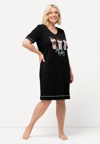 Schwarzes Nachthemd mit kurzen Ärmeln, das einen V-Ausschnitt und drei farbenfrohe Milchshake-Grafiken mit dem Text "Shake It Baby!" präsentiert. Silberner Saum am Ende.