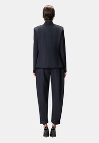 Abito blu navy a righe con blazer strutturato e pantaloni larghi. Vista posteriore con risvolti arrotolati e eleganti scarpe nere con tacco.