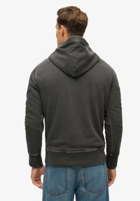 Dark gray hooded sweatshirt with textured fabric, ribbed cuffs, and hem. The back view shows stitching details and a relaxed fit.