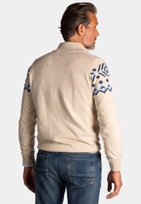 Beige poloshirt met lange mouwen en geometrische blauwe patronen op de schouders, met een kraag en geribde manchetten. Casual stof en pasvorm.