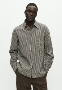 Long-sleeve button-up shirt with a brown and white vertical stripe pattern, featuring a chest pocket and a classic collar. Fabric appears textured.