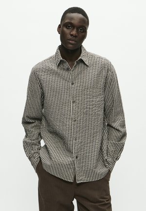 Long-sleeve button-up shirt with a brown and white vertical stripe pattern, featuring a chest pocket and a classic collar. Fabric appears textured.