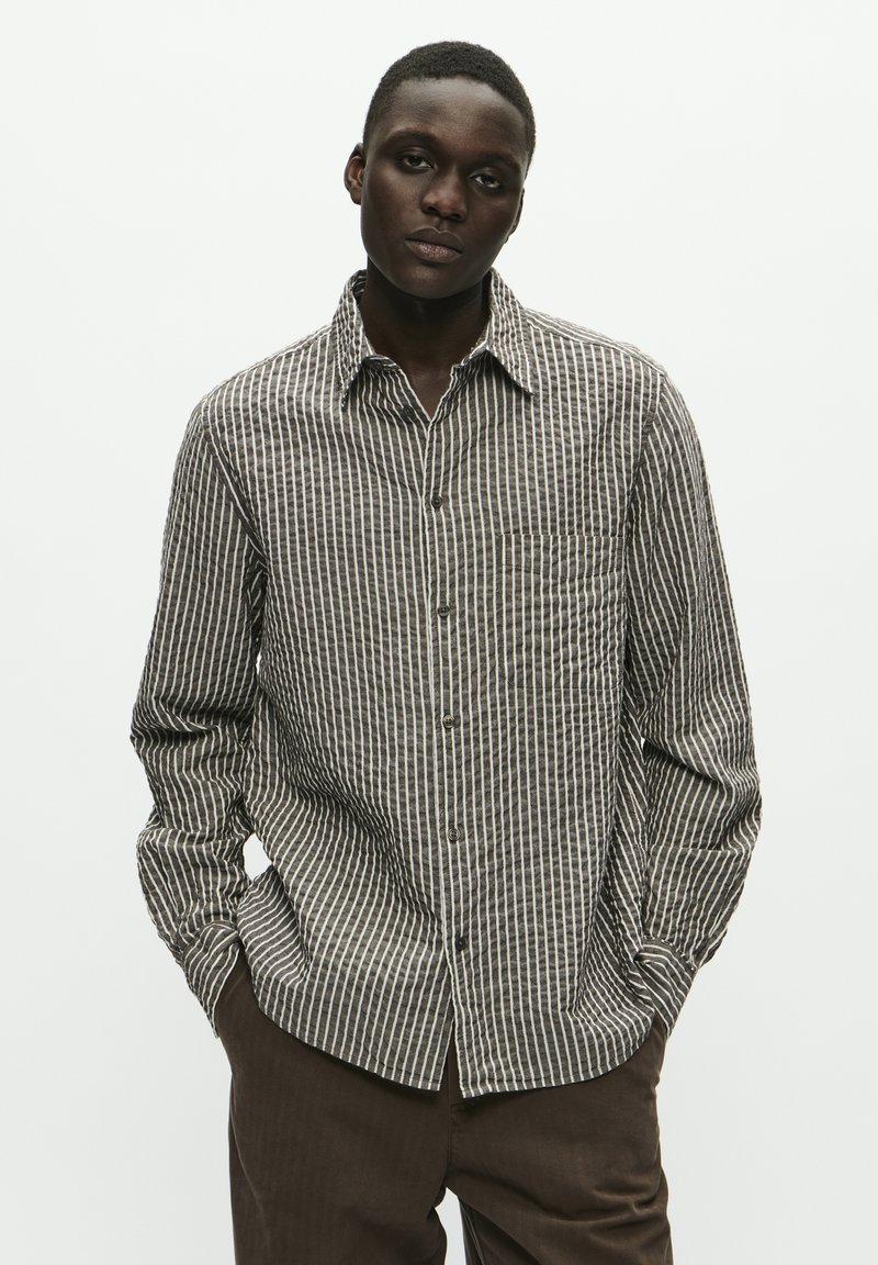 Long-sleeve button-up shirt with a brown and white vertical stripe pattern, featuring a chest pocket and a classic collar. Fabric appears textured.