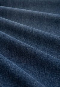 Denimstoff in tiefblau, mit glatter Textur, sichtbarem Webmuster und subtilen Farbvariationen über gefaltete Abschnitte.