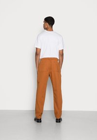 Braune Baumwoll-Cargo-Hose mit elastischem Bund, seitlichen Taschen und Gesäßtaschen. Kombiniert mit einem schlichten weißen Rundhals-T-Shirt.