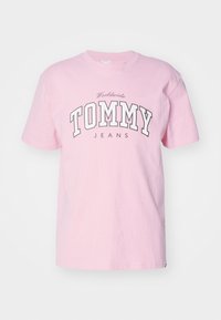 Jasnoróżowy bawełniany t-shirt z zaokrąglonym dekoltem, krótkimi rękawami oraz widocznym napisem „TOMMY JEANS” w ciemniejszych kolorach na piersi.