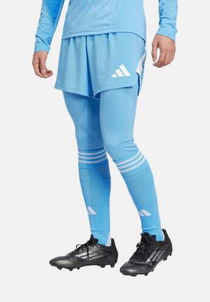 Lichtblauw sportshirt en shorts gecombineerd met bijpassende blauwe leggings met witte strepen, zwarte voetbalschoenen met een gestructureerd ontwerp en logo-accenten.