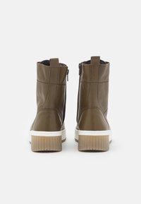 Bottes chelsea en cuir marron avec une finition texturée, fermetures éclair latérales et semelles en caoutchouc blanches. L'intérieur est doté d'une doublure en tissu doux.