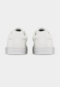 Ζευγάρι απλών λευκών sneakers χαμηλής κορυφής, εμφανίζεται από πίσω σε λευκό φόντο.