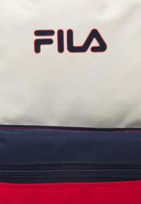 Borsa firmata Fila con superficie cremoso texturizzata, dettagli in blu navy e rosso, e chiusura a zip nella parte inferiore.