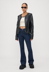 Black faux leather jacket, white cropped top, dark blue flared jeans, thick-soled black platform shoes, styled with narrow sunglasses.