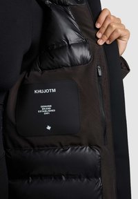 Must Black puffer vest sileda, läikev plekkvälisusega ja matte sisekattega. Omab lukuga taskut, logo kleebist ning kontrastset tekstuuri detaile.