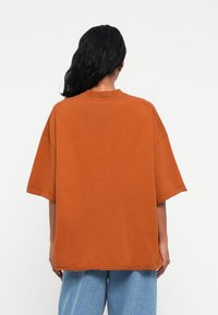 Υπερμεγέθ�η πορτοκαλί βαμβακερή μπλούζα με στρογγυλή λαιμόκοψη, κοντά μανίκια και άνετη εφαρμογή. Απλός σχεδιασμός με λεία υφή.