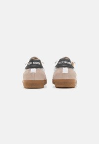 Šviesiai rudos su suede sportbačiai su juodais akcentais, turintys guminį pėdos paviršių ir "STEVE MADDEN" prekės ženklą ant nugaros. Lengvas ir tekstūruotas dizainas.