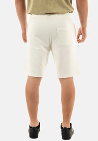 Pantaloni corti beige chiaro con vita elastica, dotati di una tasca posteriore e design a gamba dritta, abbinati a calzature nere.