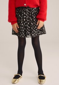 Fekete szoknya ezüst pöttyös mintával, fekete harisnyával és arany cipővel párosítva. Piros bolyhos pulóver virág gombos részletekkel.