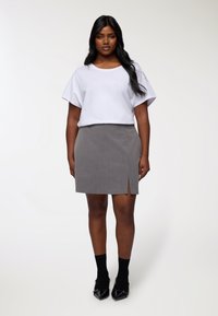 Top bianco a maniche corte abbinato a una gonna grigia a righe con uno spacco frontale, completato da calzini neri alla caviglia e scarpe nere lucide.