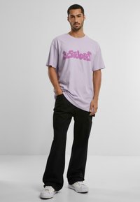 Tricou din bumbac lavandă, cu un design grafic îndrăzneț în nuanțe de roz, asortat cu pantaloni negri și adidași albi. Croială simplă, relaxată.