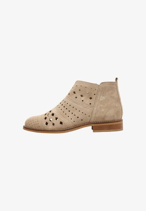 Botín beige de ante con patrones perforados de diamantes y círculos, tacón bajo de madera y tira para tirar en la parte trasera.