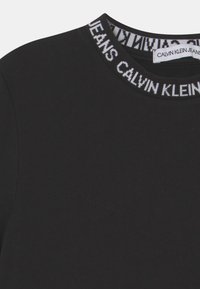 Czarna koszulka z okrągłym dekoltem z wzorem marki "CALVIN KLEIN JEANS" na prążkowanym kołnierzu oraz białą metką Calvin Klein wewnątrz dekoltu.