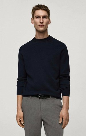 Navy blue knit sweater with a high neckline, long sleeves, and ribbed cuffs, paired with gray dress pants and a black belt.