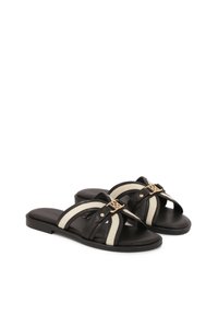 Schwarze und cremefarbene Riemchensandalen mit überkreuzten Riemen, goldfarbener Beschläge, flacher Sohle und glatter Textur. Geeignet für die Freizeit.