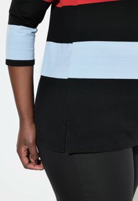 Yläosa, jossa on mustia, punaisia ja vaaleansinisiä raitoja, 3/4-hihalla ja sivuhalkio. Sileä rakenne, kevyt kangas. Yhdistetty mustiin legginsseihin.