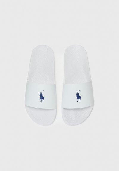 Vita sandaler i vitt med en texturerad sula och en bred rem som har en marinblå polo-spelare som logotyp. Hållbart material, minimalistisk design.