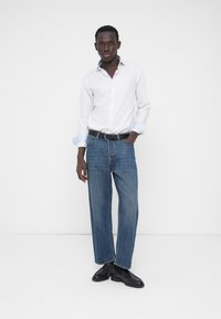 Weißes Langarmhemd mit hellblauen Manschetten, kombiniert mit locker sitzenden blauen Jeans und schwarzen Lederschuhen. Schlichtes Design, entspannte Passform.