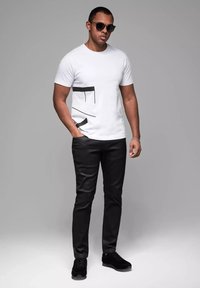 Camiseta blanca de manga corta con diseño gráfico negro en la parte frontal, combinada con pantalones ajustados negros y zapatillas negras.