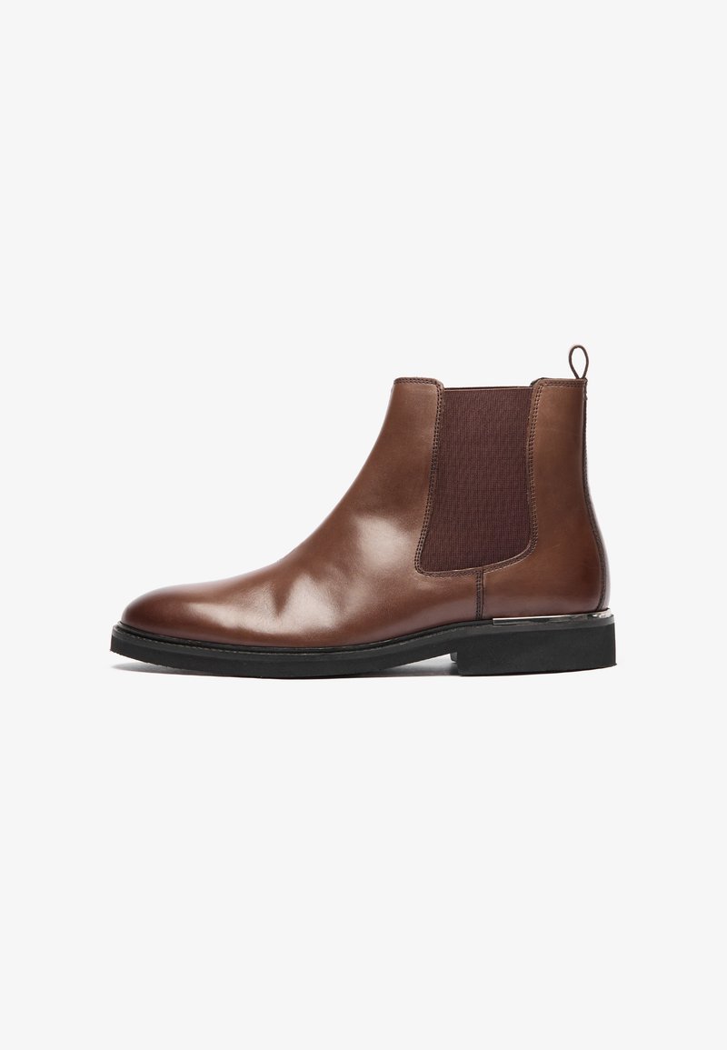 Bota Chelsea de cuero marrón con paneles laterales elásticos, punta redondeada, tirador y un acabado texturizado. Suela de goma negra para mayor agarre.
