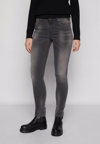 Jeans skinny cinzentos feitos de denim com ligeira descoloração. Apresentam um design clássico de cinco bolsos e um ajuste justo, combinados com botas de tornozelo pretas.