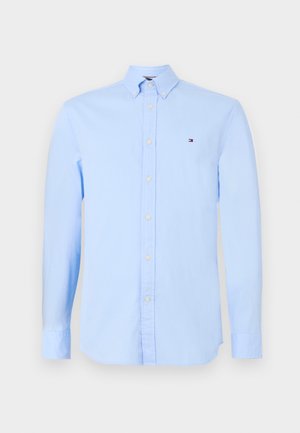 Lyseblå skjorte med knapp, laget av bomull, med spiss krage, lange ermer og en liten brodert logo på brystet.