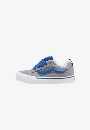 Zapatilla de ante gris con acentos azules, suela de goma blanca y cordones azules. Cuenta con un diseño de rayas característico y un collar acolchado para mayor comodidad.