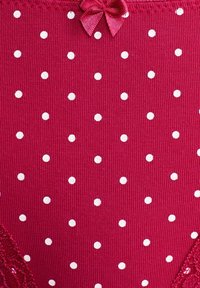 Tissu rouge à pois blancs. Présente une texture côtelée et un petit nœud en ruban accentuant la taille. Détail en dentelle sur un côté.