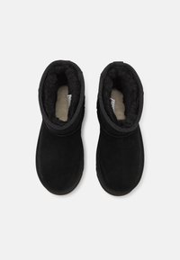 Čierne ankle boots vyrobené z semišu s mäkkou, plyšovou podšívkou. Obsahujú skladací golier a plochú gumovú podrážku pre pohodlie.