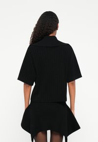 Μαύρο πλεκτό πουλόβερ με κοντά μανίκια και ψηλό γιακά, διαθέτοντας σχέδιο καμπύλης στο τελείωμα. Το υφαντό ύφασμα προσφέρει ευέλικτη εφαρμογή.