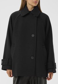 Black wool blend coat featuring a wide collar, black buttons, and two side pockets. The design includes a loose fit and cuffed sleeves.