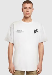 Hvid oversized t-shirt med korte ærmer. Har grafisk tekst i sort på fronten og højre side. Blødt bomuldsstof.