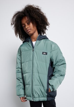 Cazadora acolchada en verde con detalles en negro, presenta un cierre de cremallera, capucha, puños de canalé y es ligera con una textura suave.