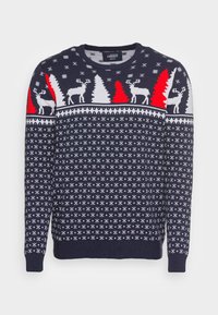 Pull en tricot bleu marine avec des rennes et des arbres blancs, agrémenté d'accents rouges. Le motif comprend des flocons de neige et des dessins géométriques.