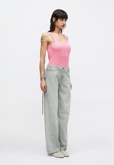Ροζ ριμπ τιράντα συνδυασμένη με ανοιχτό γκρι τζιν παντελόνι φαρδιάς γραμμής με κούμπωμα με κουμπί και λεπτομέρεια δέστρας στο πλάι, φορεμένα με παπούτσια σε απαλό γκρι χρώμα.