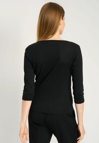 Czarny, długi rękaw top z okrągłym dekoltem, prążkowaną fakturą i dopasowanym krojem. Noszony z czarnymi spodniami, widok z tyłu.