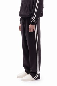 Μαύρα παντελόνια φούτερ με δύο κάθετες λευκές ρίγες στα πλάγια. Κατασκευασμένα από μαλακό ύφασμα, διαθέτουν ελαστική μέση και ένα μικρό λογότυπο.