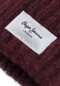 Burgundska pletena tkanina s teksturiranim završetkom, koja sadrži bijelu šivanu oznaku s natpisima "Pepe Jeans" i "London" u crnom tekstu.