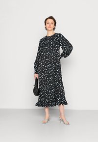 Vestido preto com bolinhas azuis claras, mangas longas, bainha com babados, feito de tecido suave; combinado com sandálias de tira azul claras.