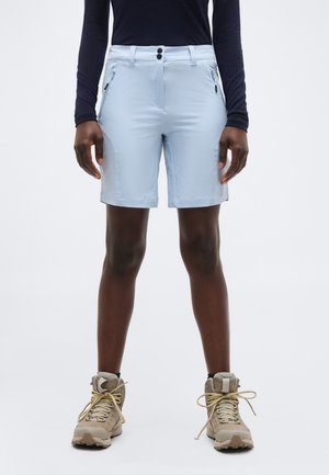 Osoba ubrana w jasnoniebieskie szorty do kolan z zamykanymi na zamek bocznymi kieszeniami, czarną bluzę z długim rękawem oraz beżowe buty trekkingowe.