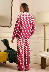Ensemble de pyjama bordeaux avec des motifs de cœurs blancs. Le haut à manches longues et le pantalon assorti ont une coupe décontractée avec des accents de bordure contrastants.