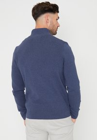 Marineblauer Pullover aus feinem Strickstoff. Verfügt über einen hohen Kragen, lange Ärmel sowie gerippte Bündchen und Saum. Keine sichtbaren Muster.