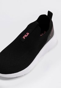 Svart slip-on sneakers med en andningsbar mesh-övre, vit sula och rosa branding på sidan och tungan. Texturerad yta med dragflik.